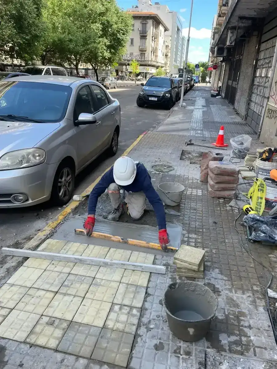 Operario colocando baldosas de vereda y nivelándolas con regla