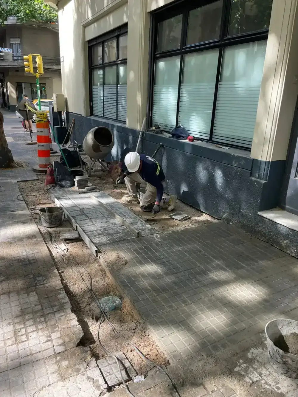 Operarios colocando baldosas de vereda al pie del frente del edificio