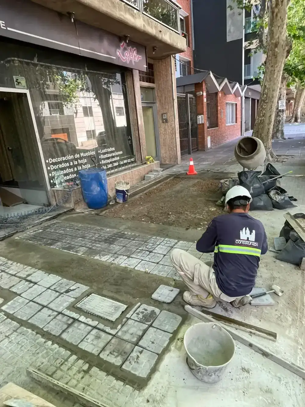 Operario colocando baldosas de vereda frente a un local comercial